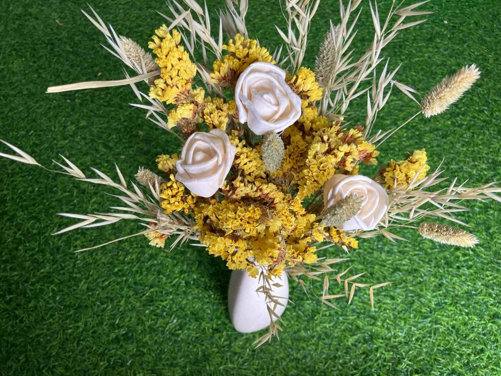 A vibrant dried yellow flowers bouquet featuring statice, sola wood roses, and bunny tails in a rustic vase
