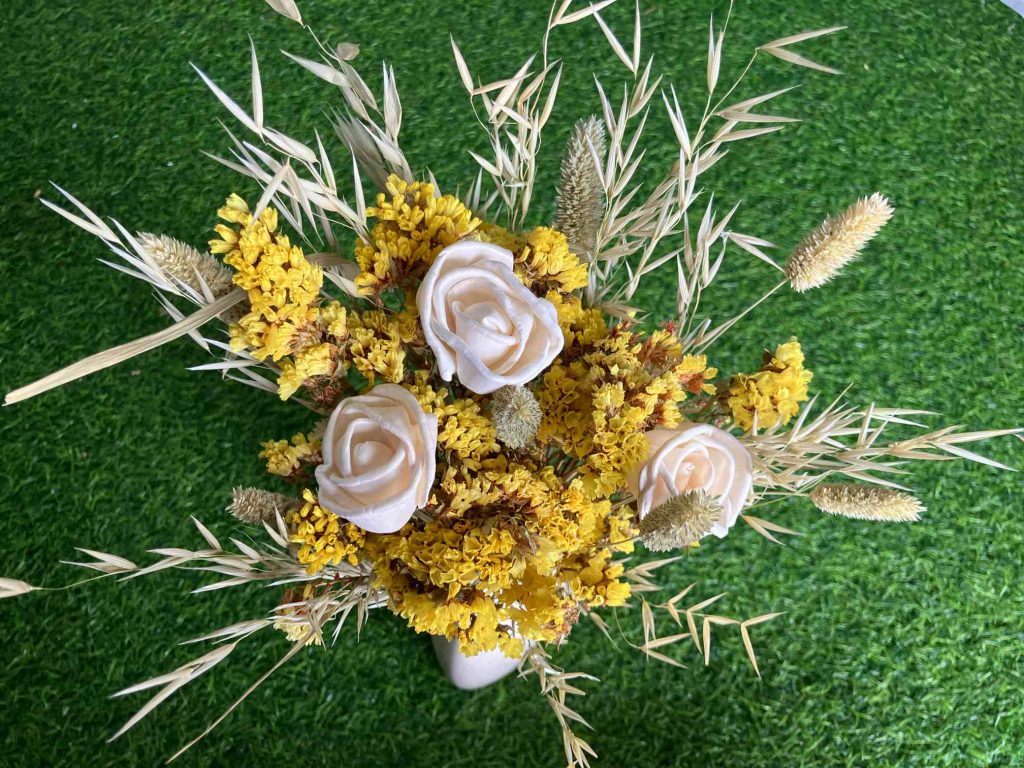 A vibrant dried yellow flowers bouquet featuring statice, sola wood roses, and bunny tails in a rustic vase