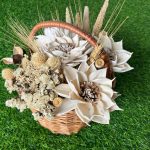 Natural dried flower basket arrangement with millet sprays, wheat grass, white statice, and cotton pods on wooden table